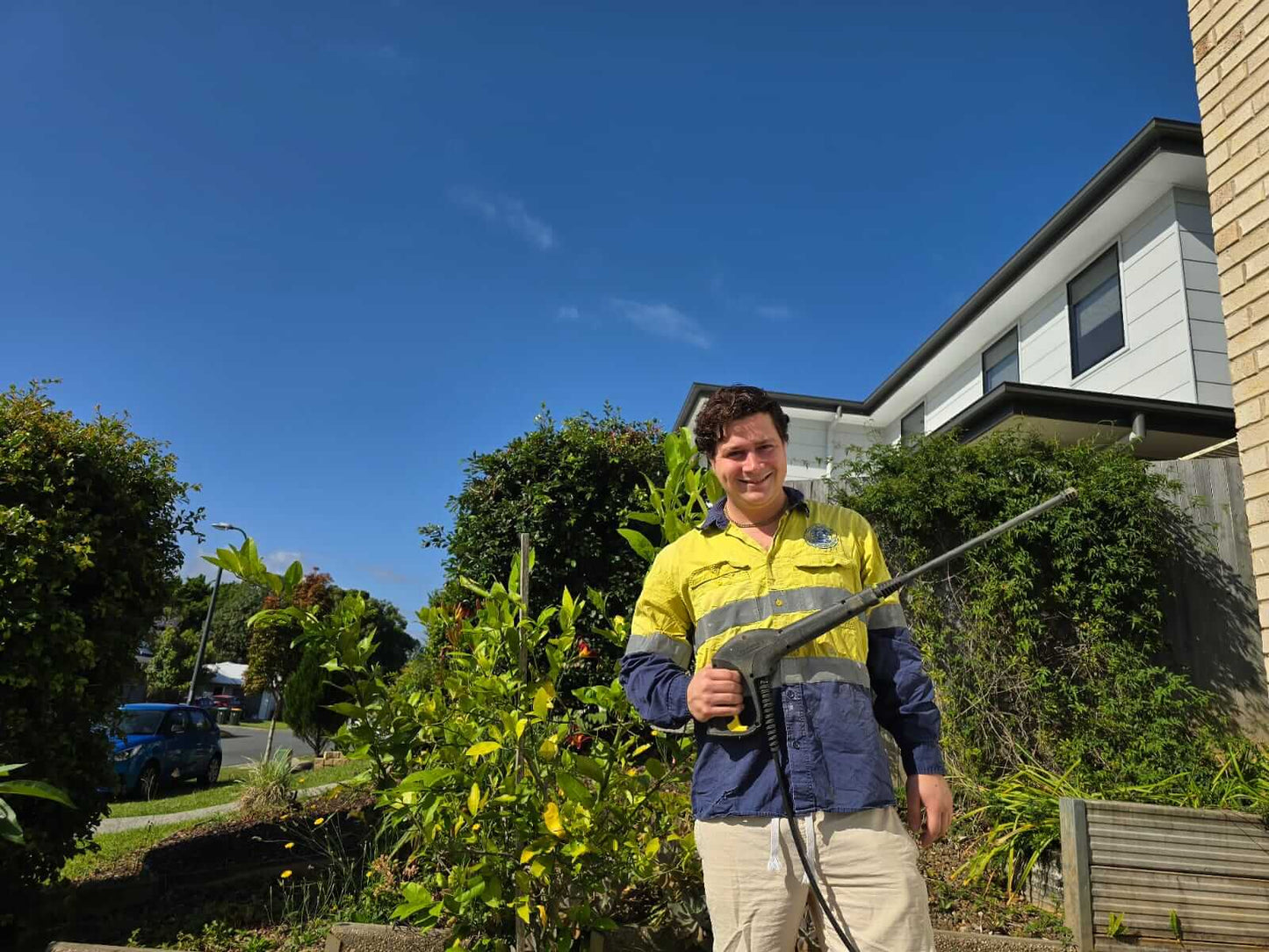A person standing outside with pressure washing equipment, with a residential area in the background.